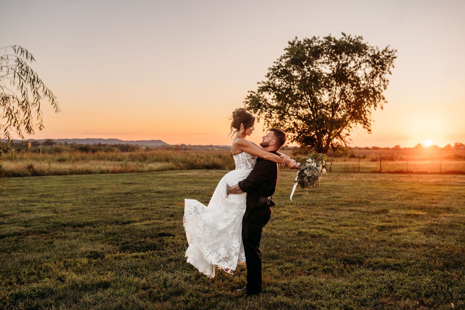 Romantic wedding couple embraces in a golden field at sunset with dramatic lighting.