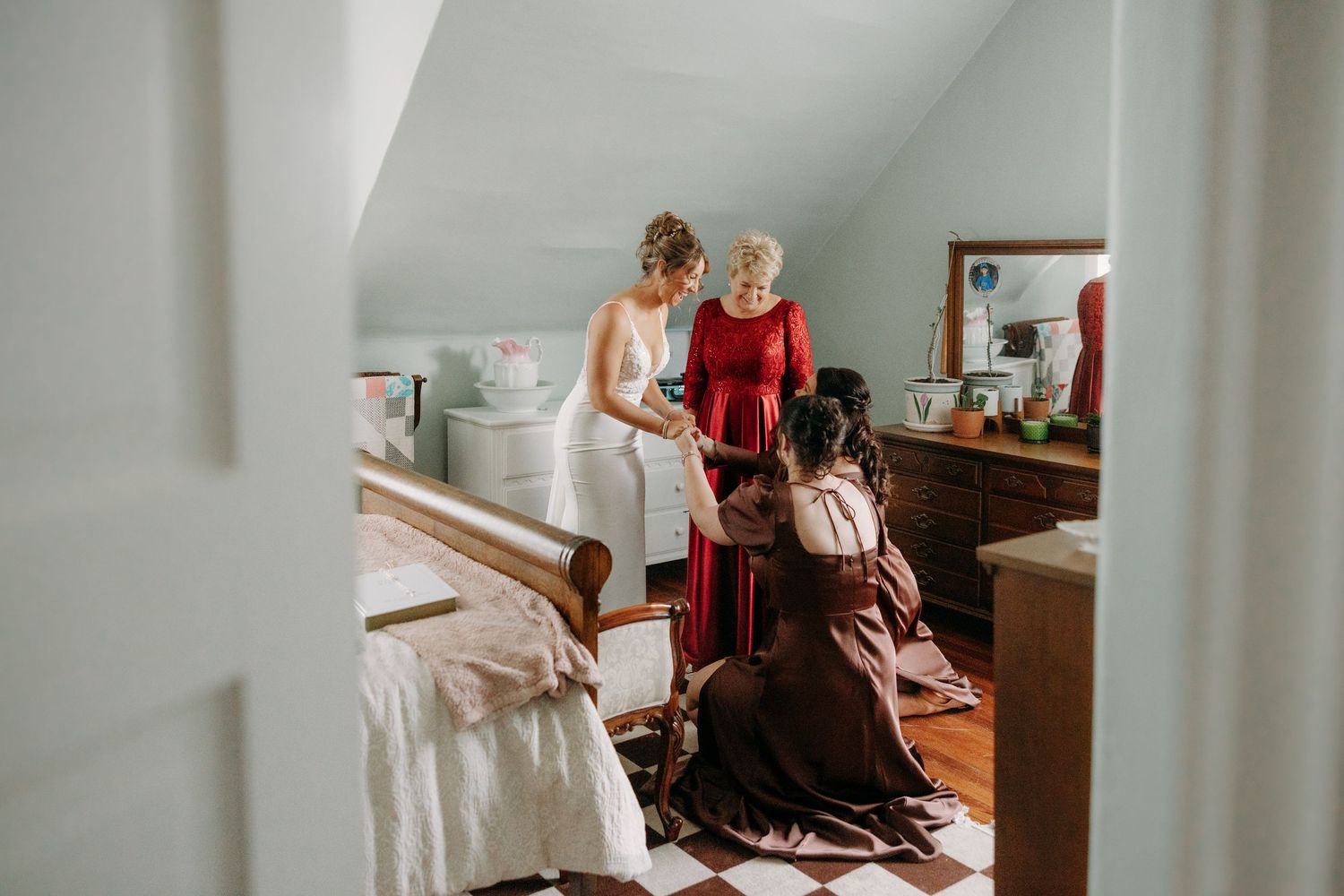 Bride being helped into wedding dress by family members in a charming attic bedroom.