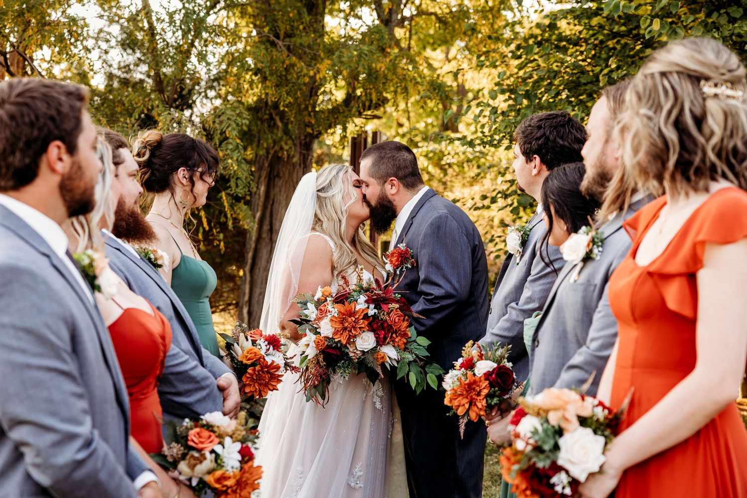 A wedding ceremony moment surrounded by guests in an outdoor garden setting with autumn trees.