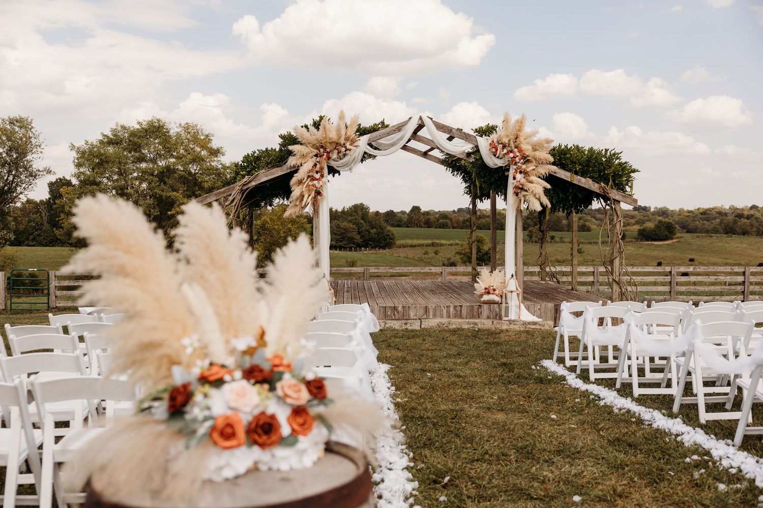 Outdoor wedding ceremony setup with white chairs and floral arch decorations.