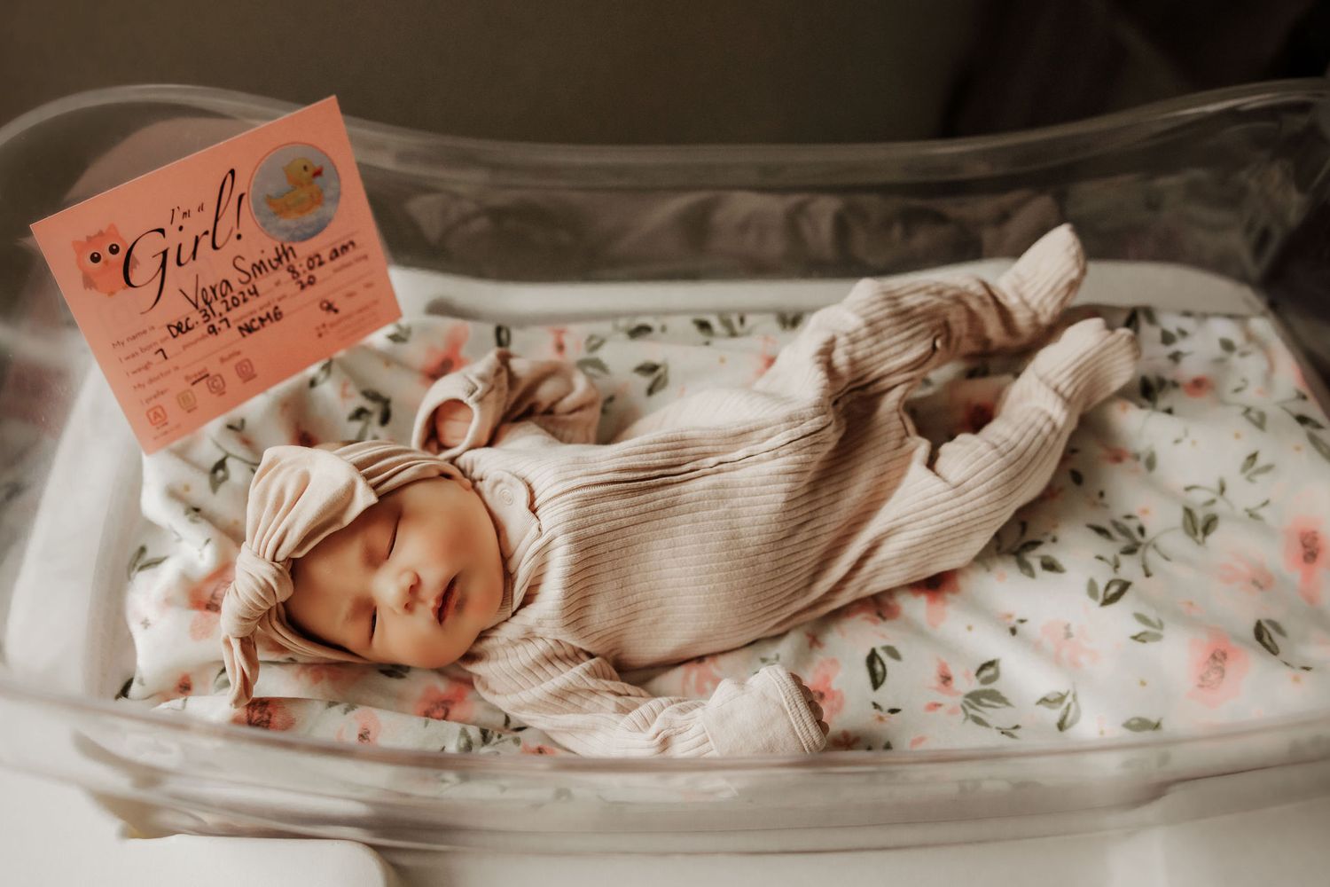 Newborn baby in knit outfit lying in hospital bassinet with identification card.