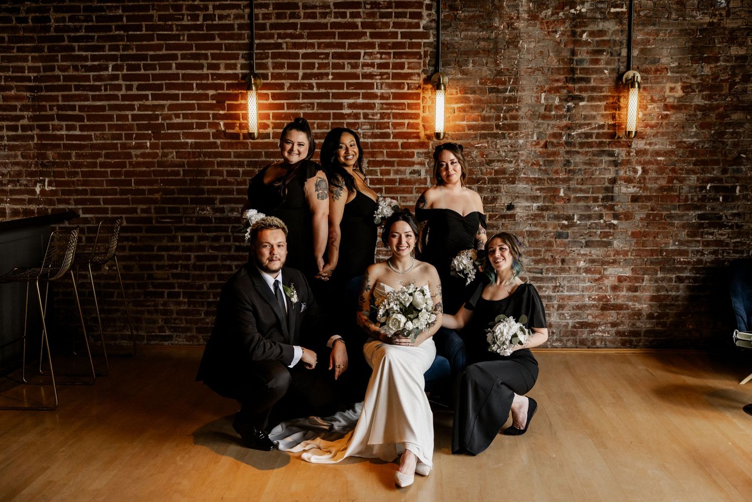 Wedding party poses together against exposed brick wall with industrial lighting at The Frazier History Museum.