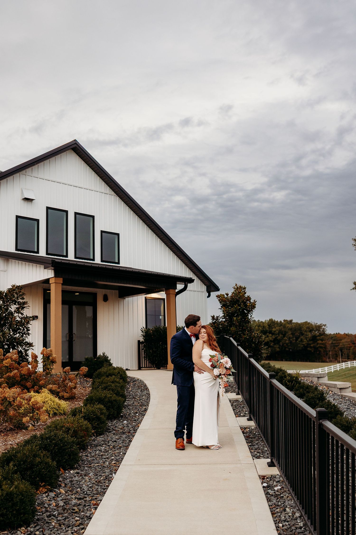 Modern white farmhouse style wedding venue with black railings against cloudy sky. Phillips Grove, Radcliff, KY.