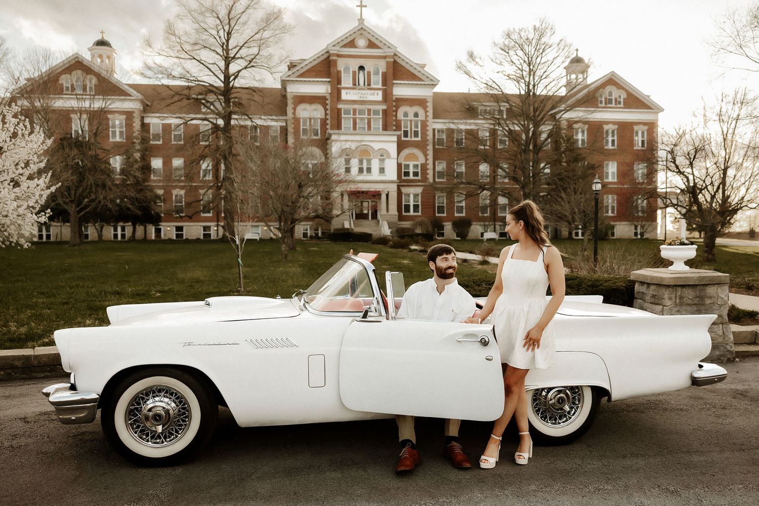 Vintage white convertible car parked in front of a historic brick building.