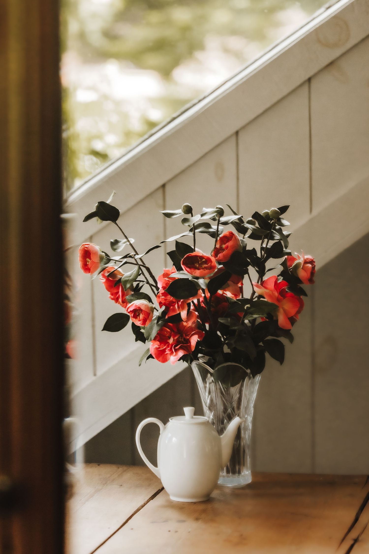 Red coral flowers in white vases arranged under slanted ceiling with natural lighting.