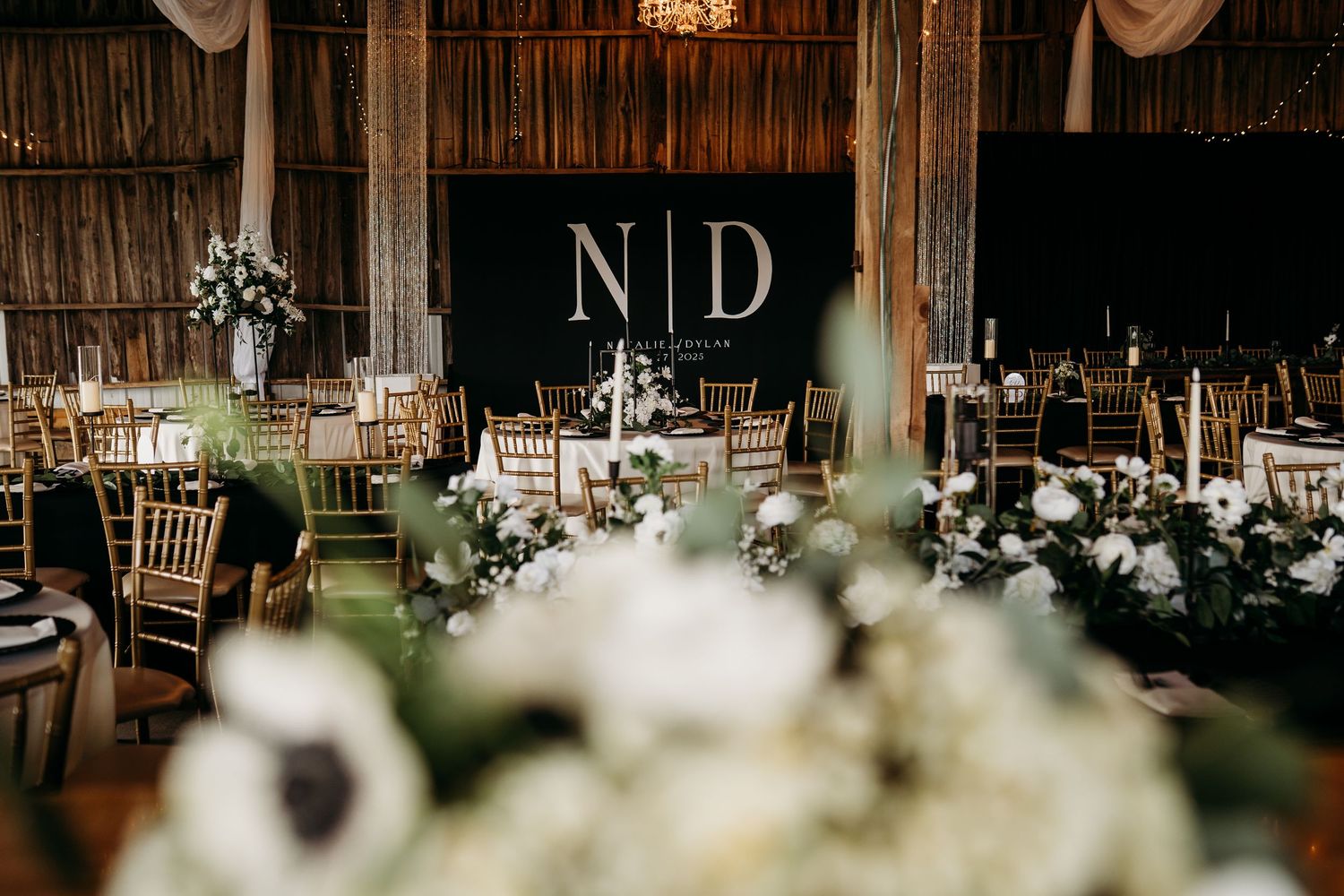 A decorated barn wedding reception space with white drapery and floral arrangements.