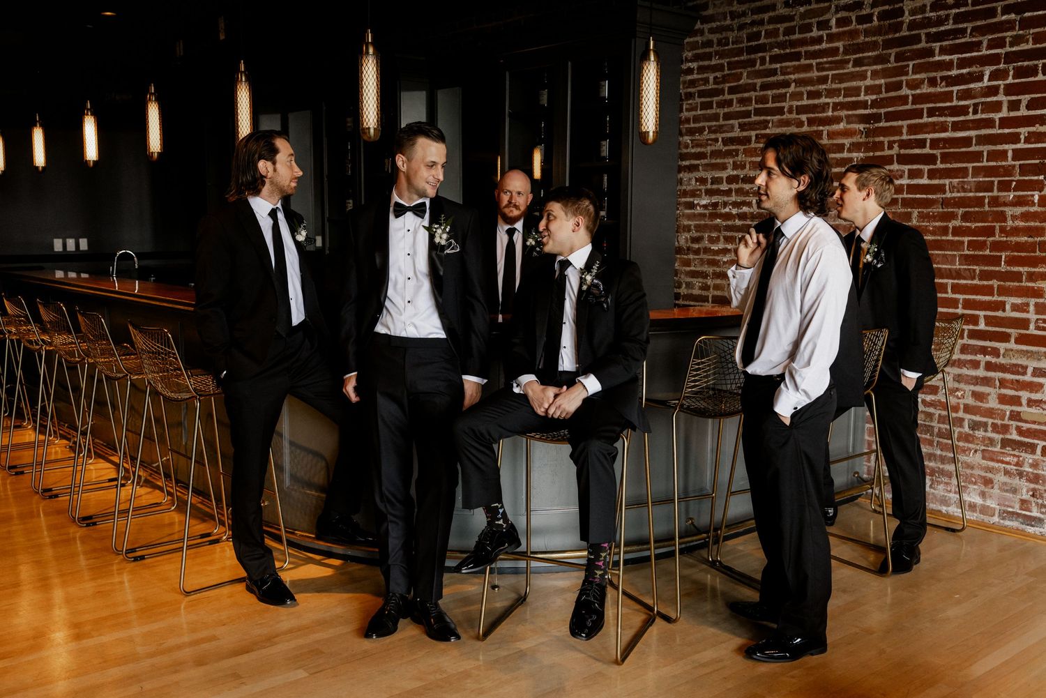 Candid shots of groomsmen interacting in rustic brick venue with pendant lights.