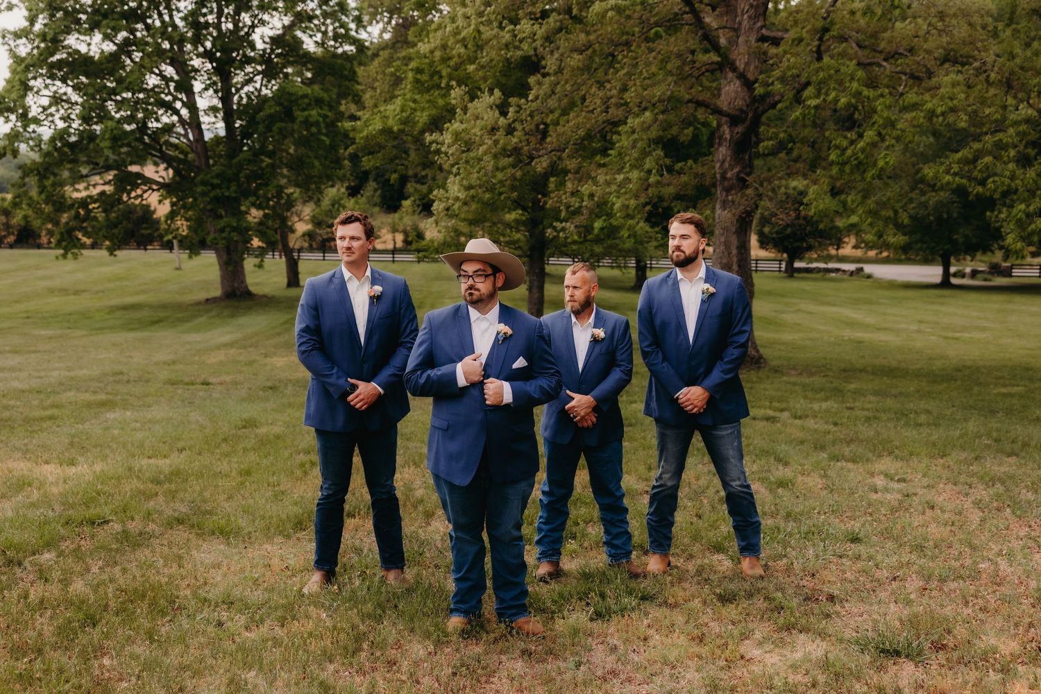 Groom and groomsmen in navy blue suits posing outdoors on green grass at a wedding celebration.