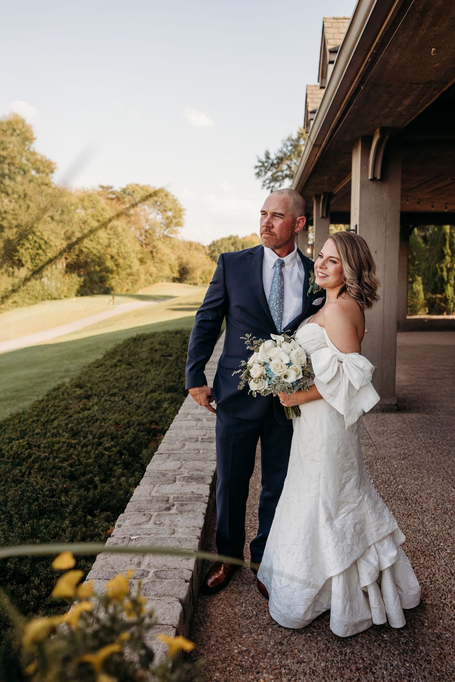 Couple poses under stone archway during wedding photoshoot.