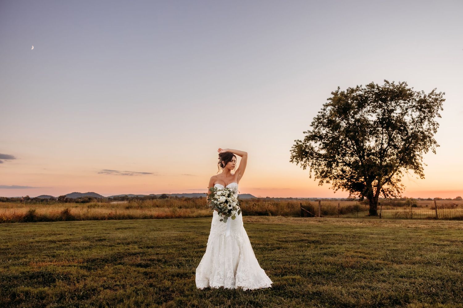 Stunning sunset wedding photos taken in an open field with a lone tree silhouetted against the colorful sky.