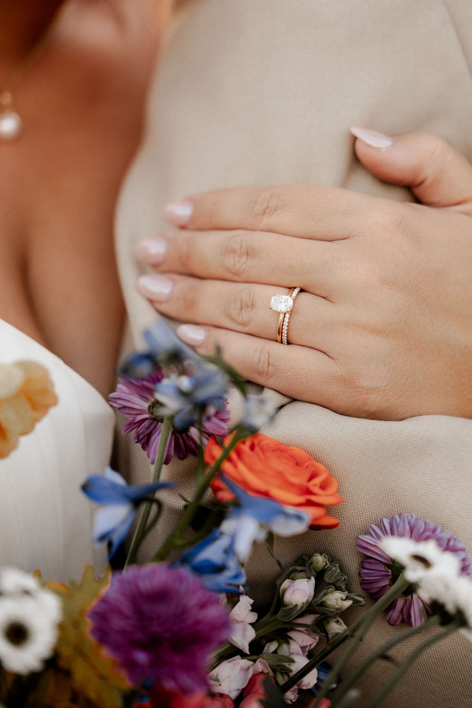 Close-up of wedding ring and colorful floral bouquet with purple and orange blooms.