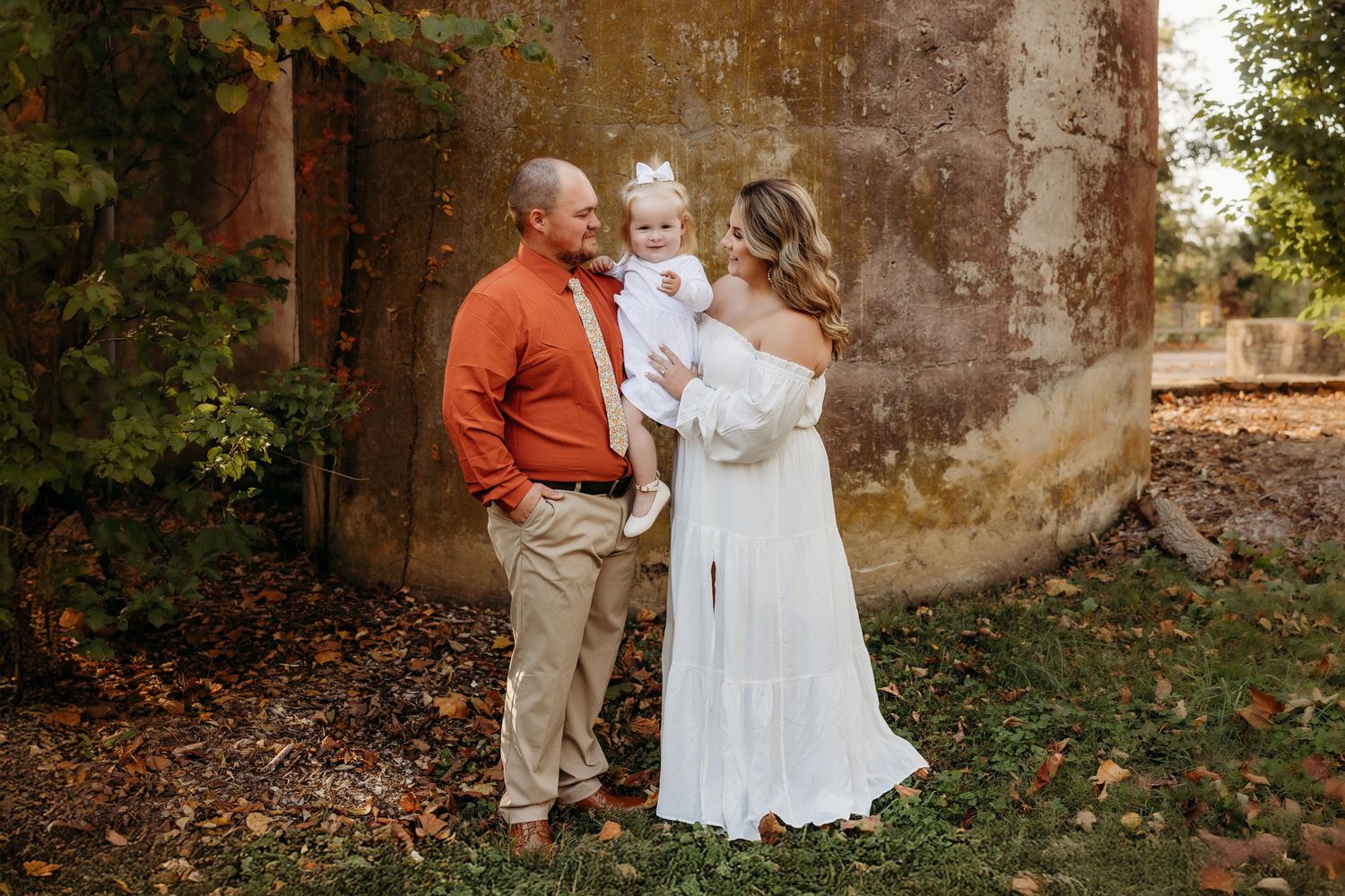 Outdoor portrait session against weathered stone wall surrounded by autumn foliage.