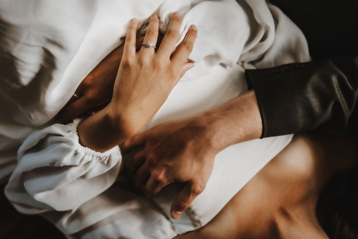 A series of intimate close-up shots showing hands gently touching white fabric in dramatic lighting.