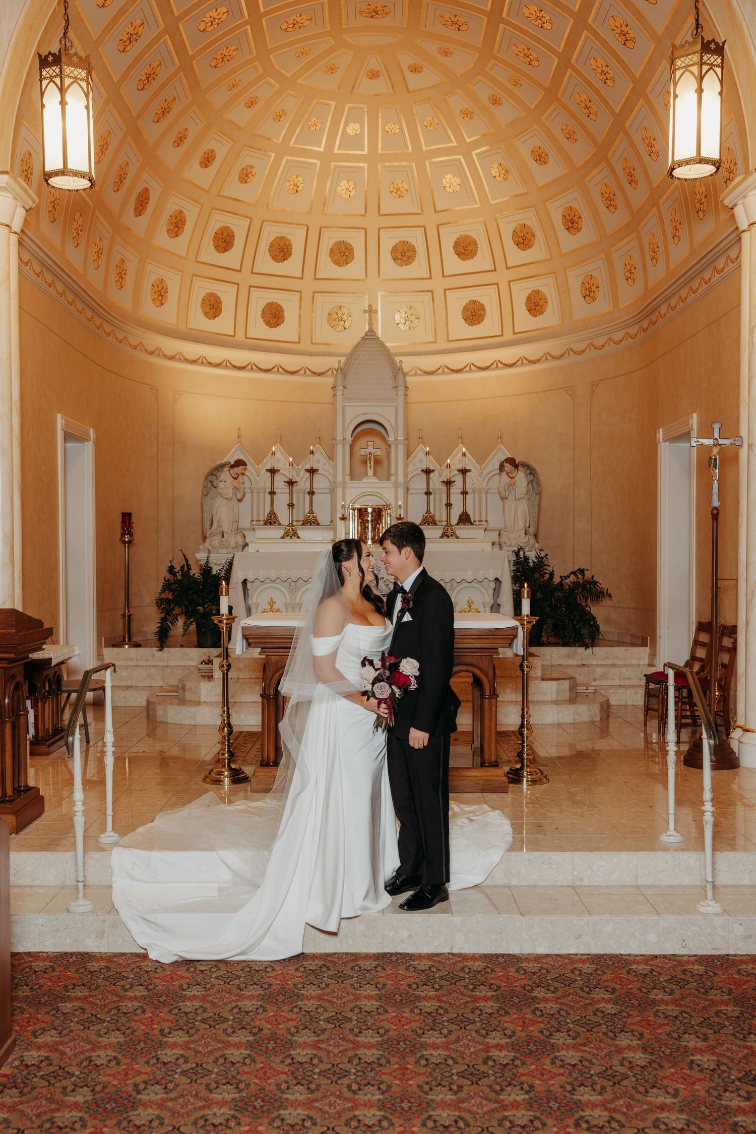 Bride and groom share a kiss at ornate church altar beneath a stunning gilded dome ceiling.
