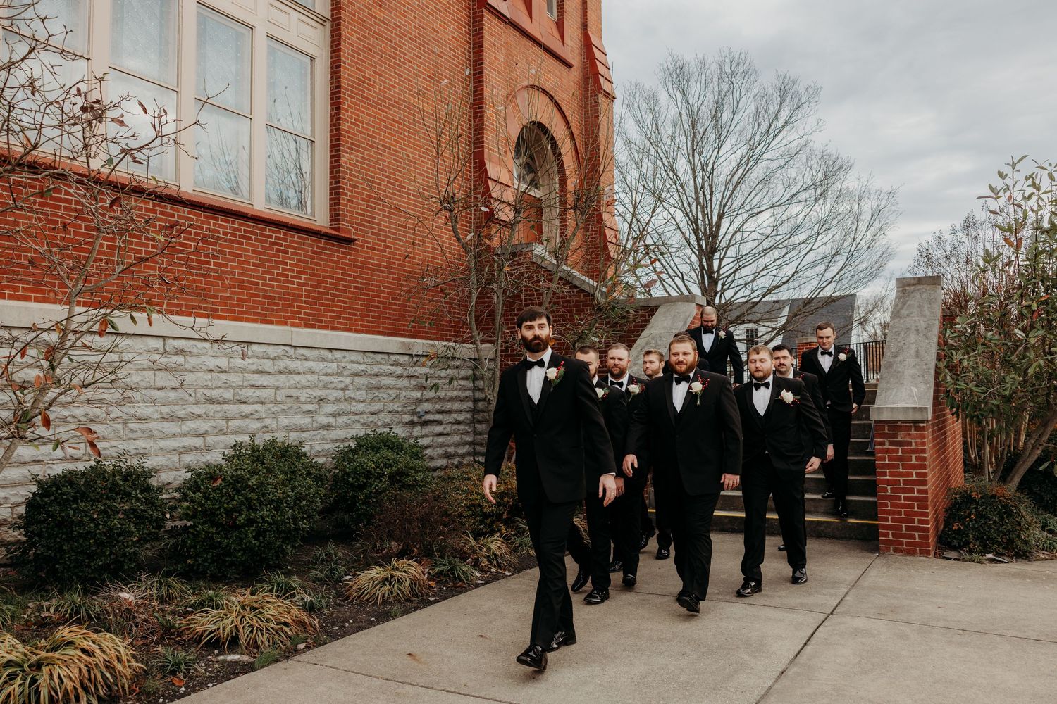 Wedding party members in black attire pose on brick church steps.