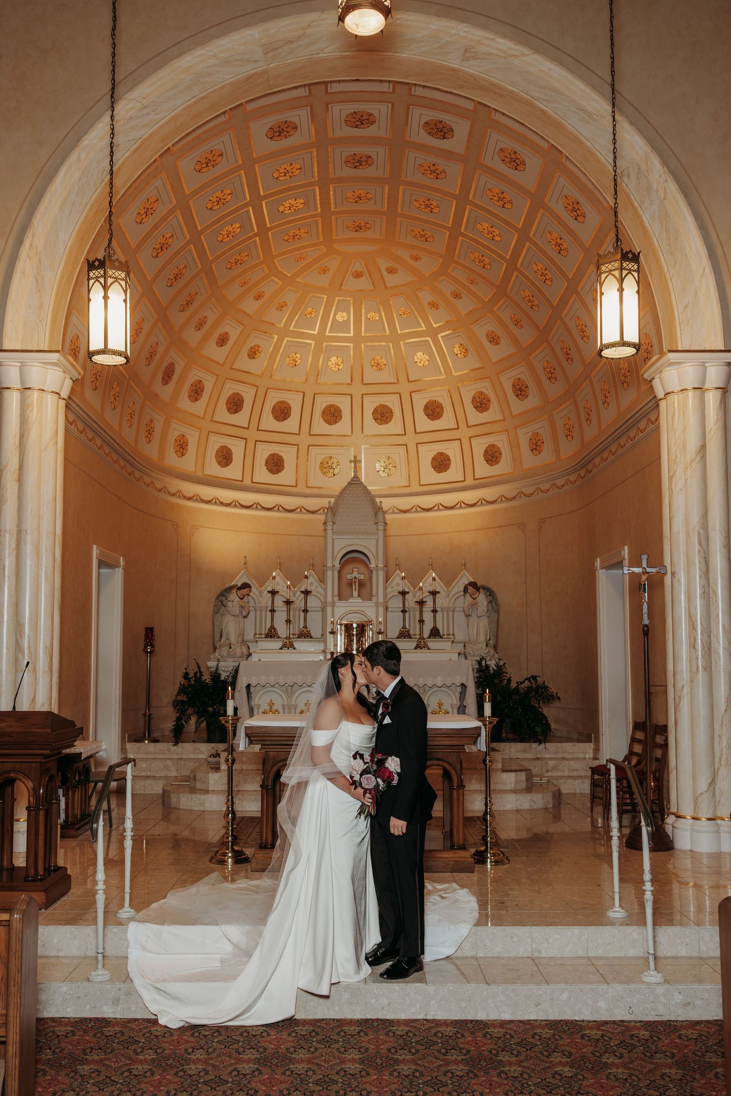 Wedding ceremony taking place in an elegant catholic church with ornate domed ceiling and classical architecture.
