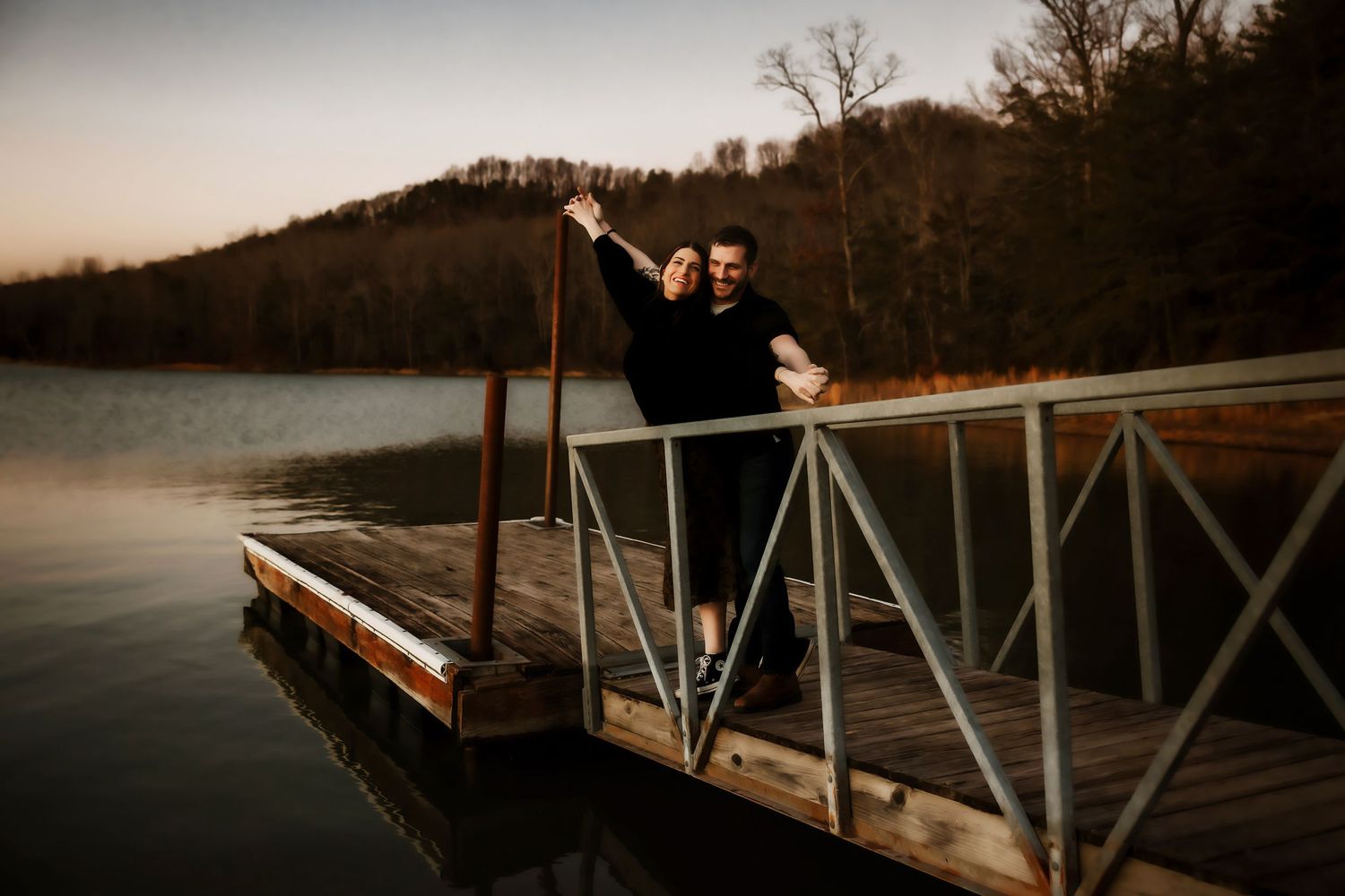 Scenic lakeside dock at sunset with mountains in the background.