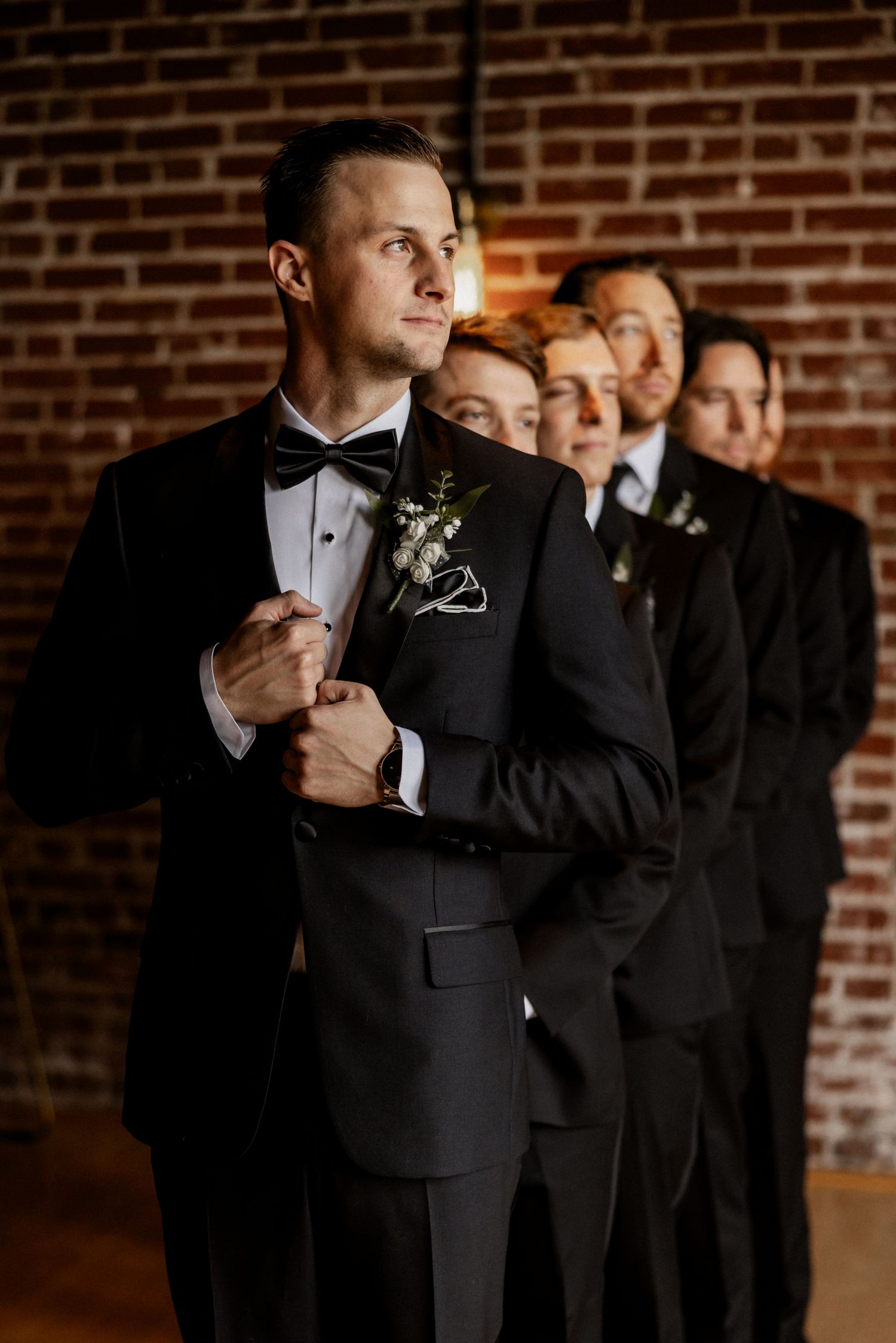 Close-up sequence of groomsmen adjusting bowties and suits against brick wall.