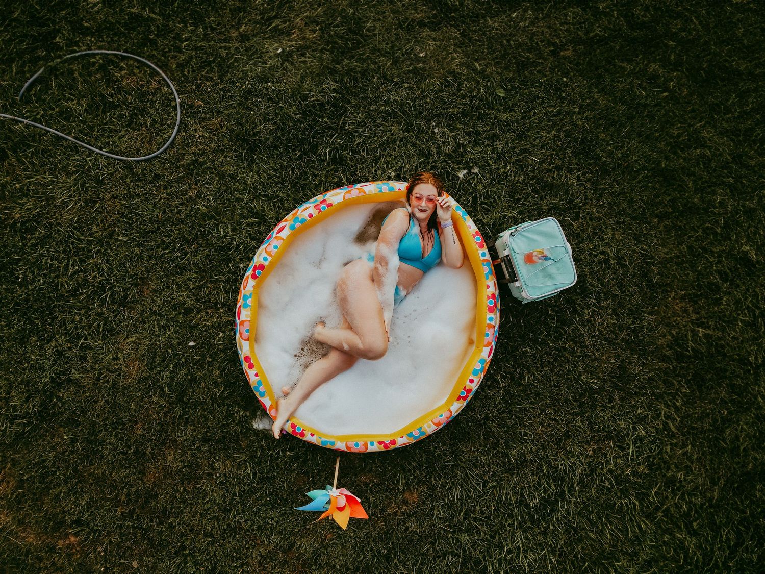 A colorful inflatable pool on grass with summer accessories and toys scattered around.