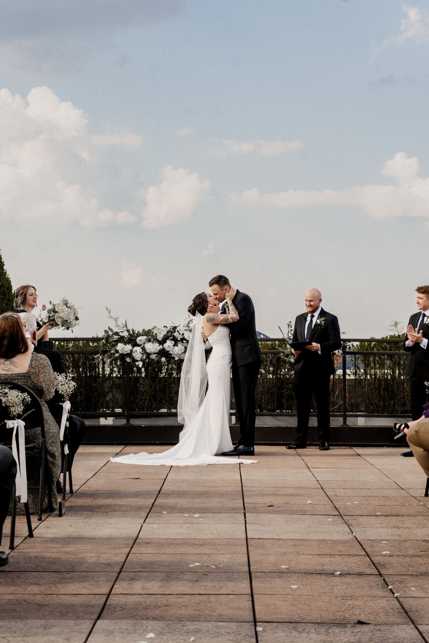 Newlyweds share first kiss during outdoor wedding ceremony while guests look on at Frazier History Museum