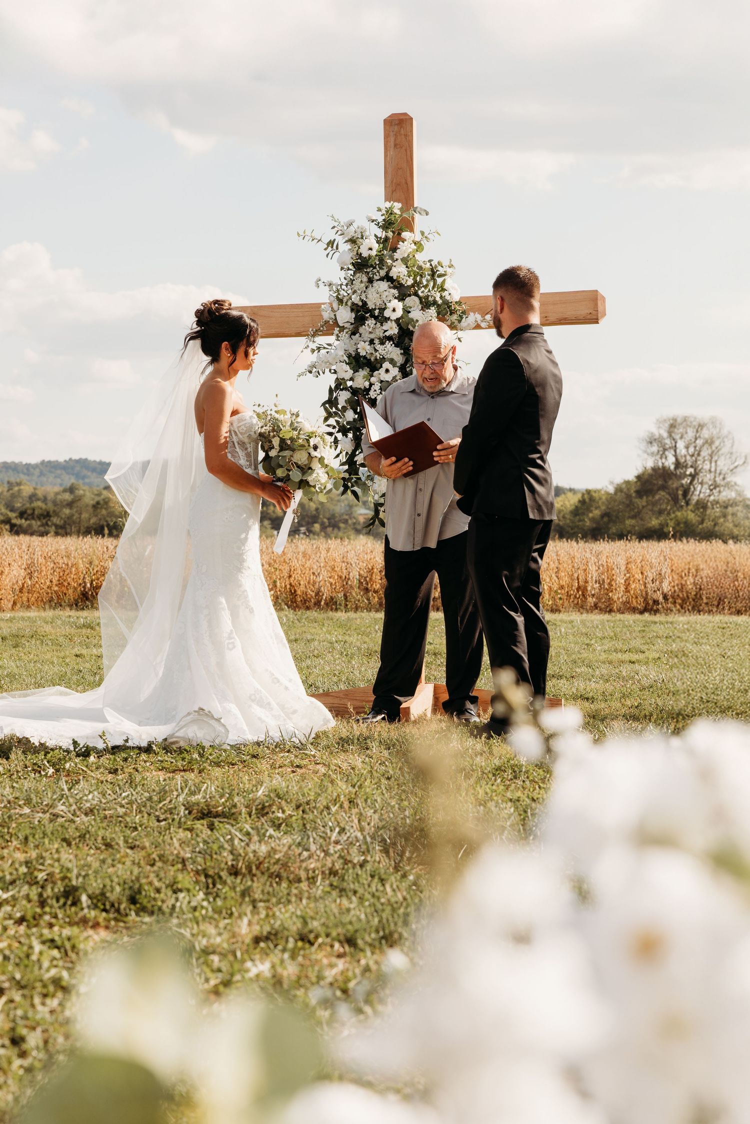 Outdoor wedding ceremony setup with wooden cross and wildflowers in rustic Kentucky field setting.