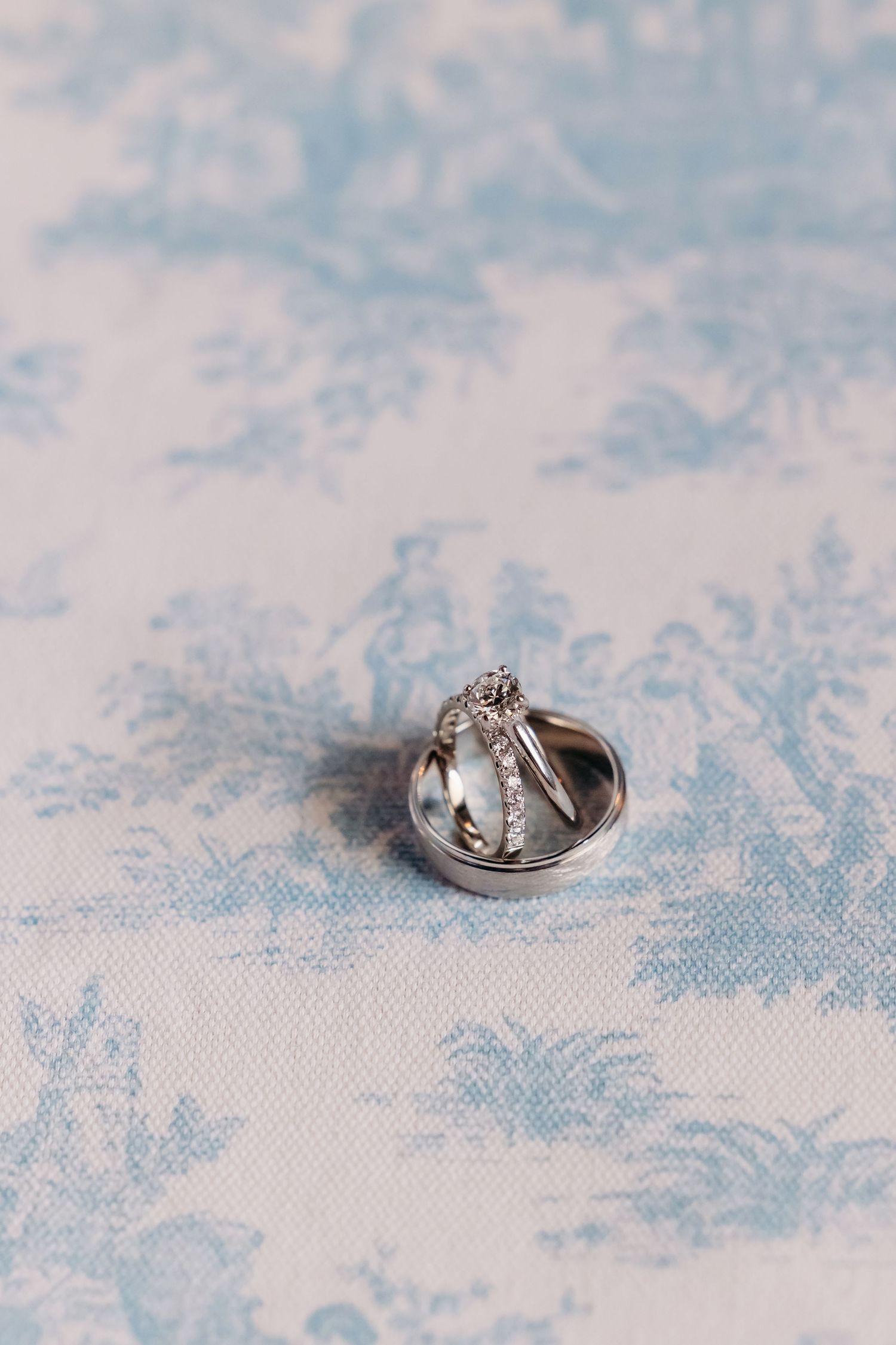 Three wedding rings stacked together on a blue and white toile fabric background.