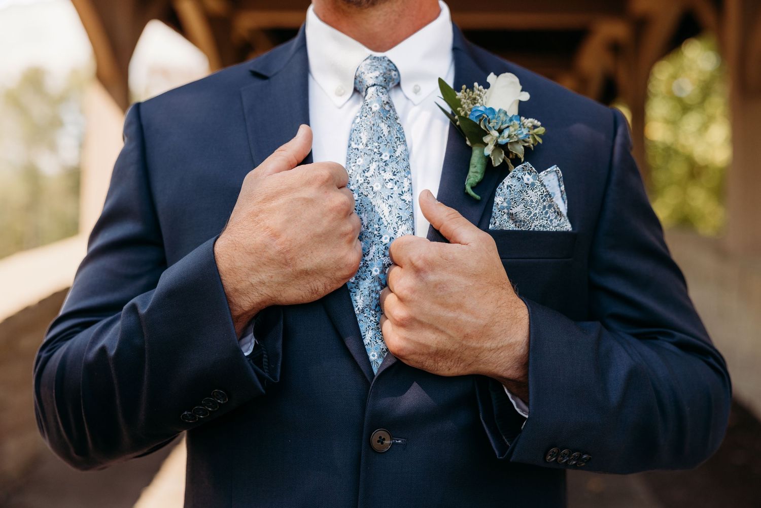 Close up details of Groom with navy blue suit and light blue patterned tie.
