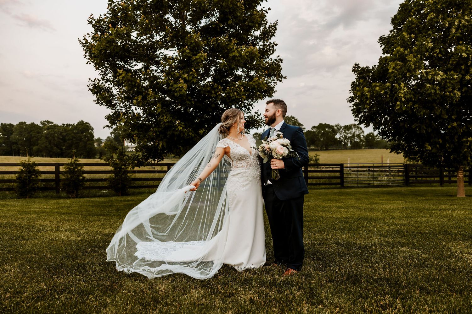 A flowing white wedding veil catches the breeze in an open field during golden hour at The Venue at Evan's Orchard.