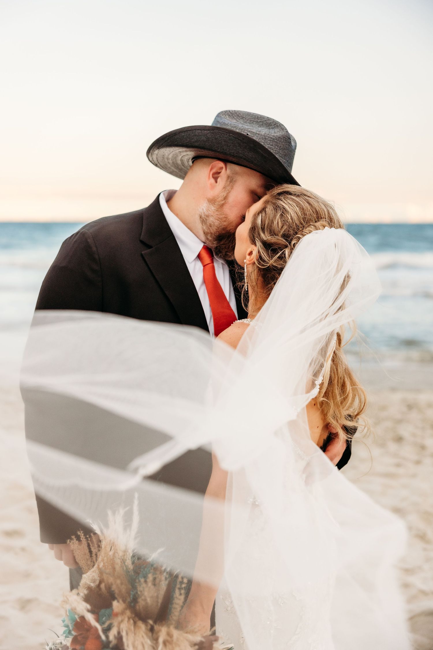 Romantic beach wedding portraits with flowing veil against ocean backdrop.