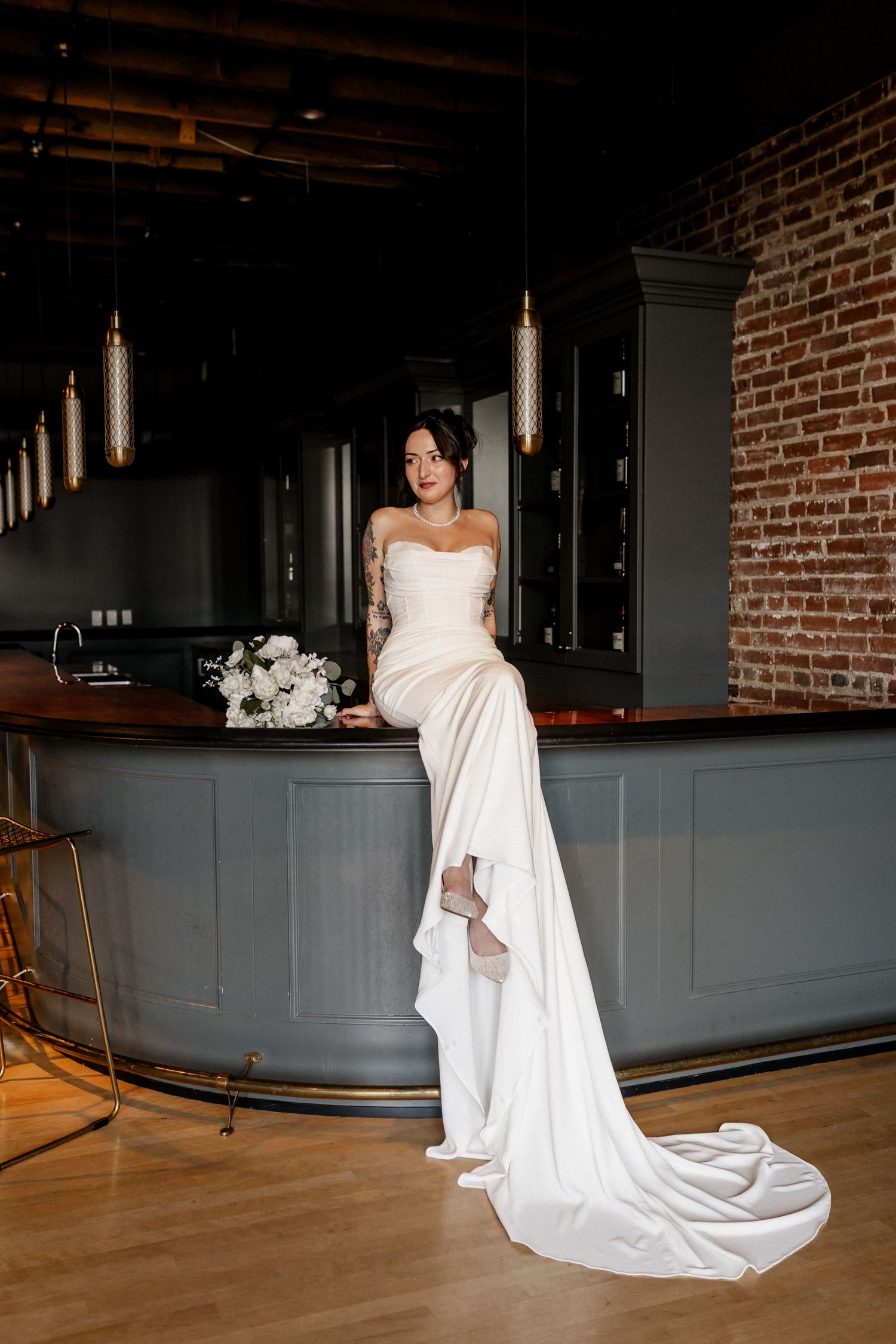 Bride sitting on the bar in a modern wedding venue with exposed brick walls.