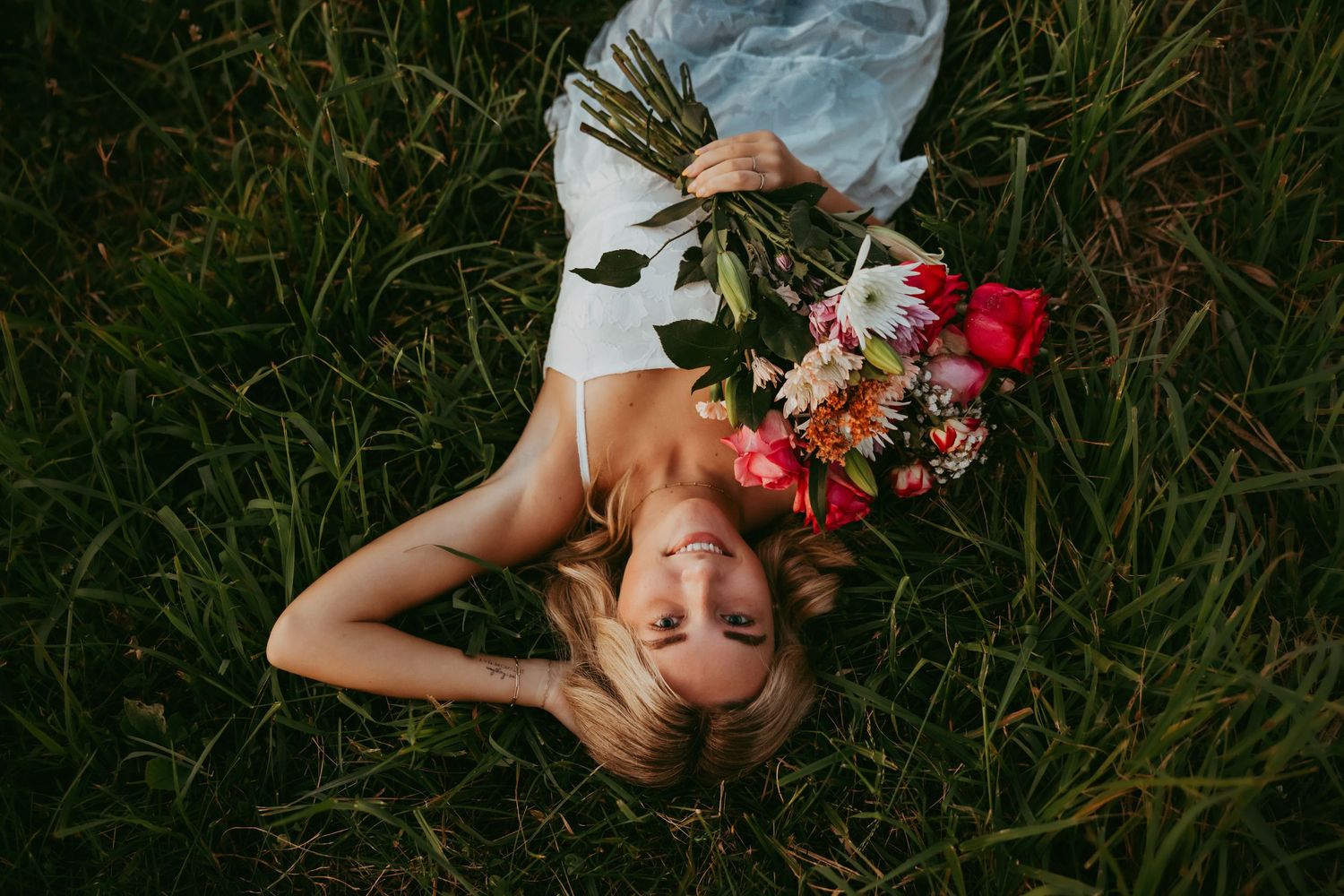 Artistic overhead shot of person lying in grass holding colorful flower bouquet.
