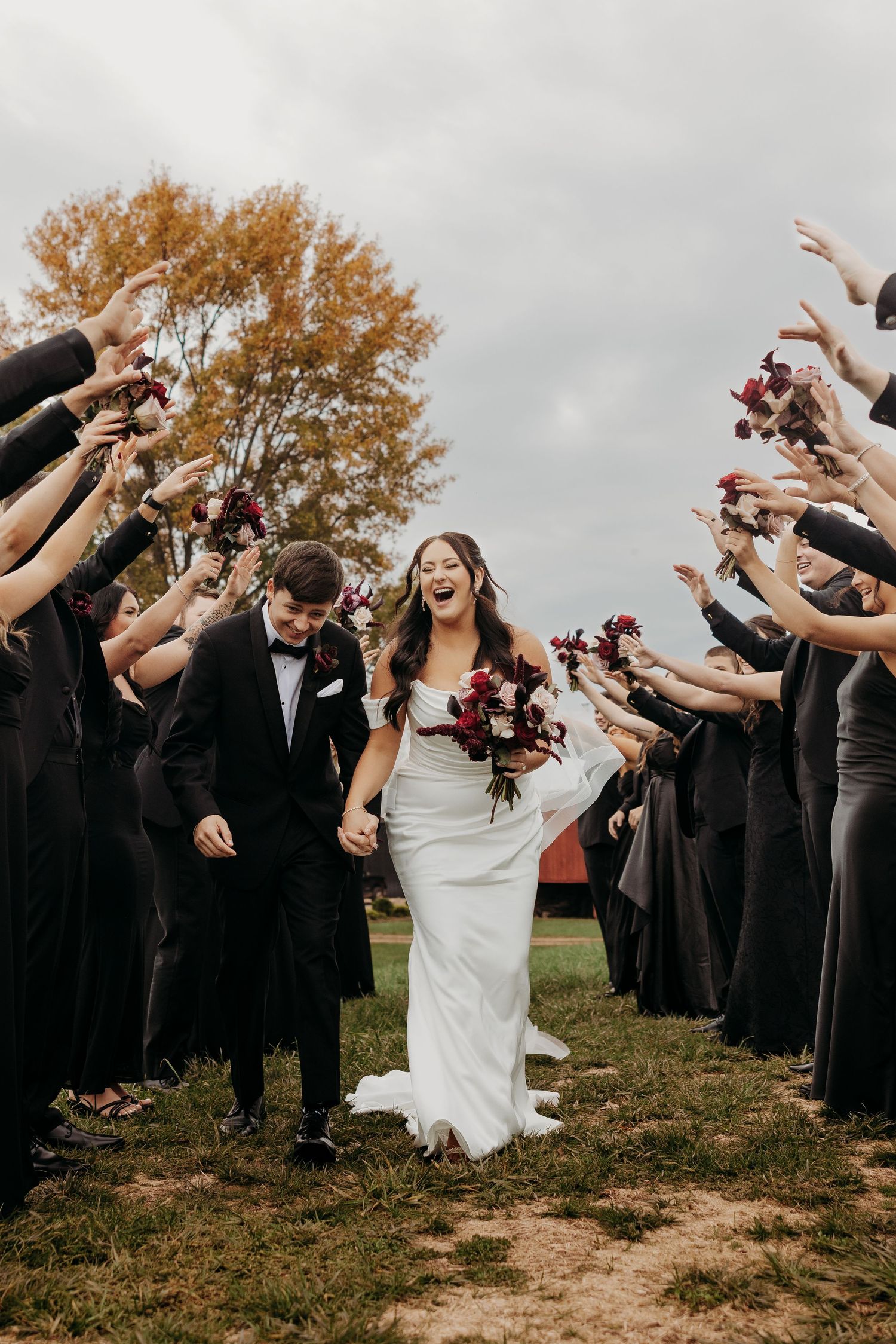 Wedding party forms a celebratory tunnel as newlyweds walk through with guests raising hands in joy.