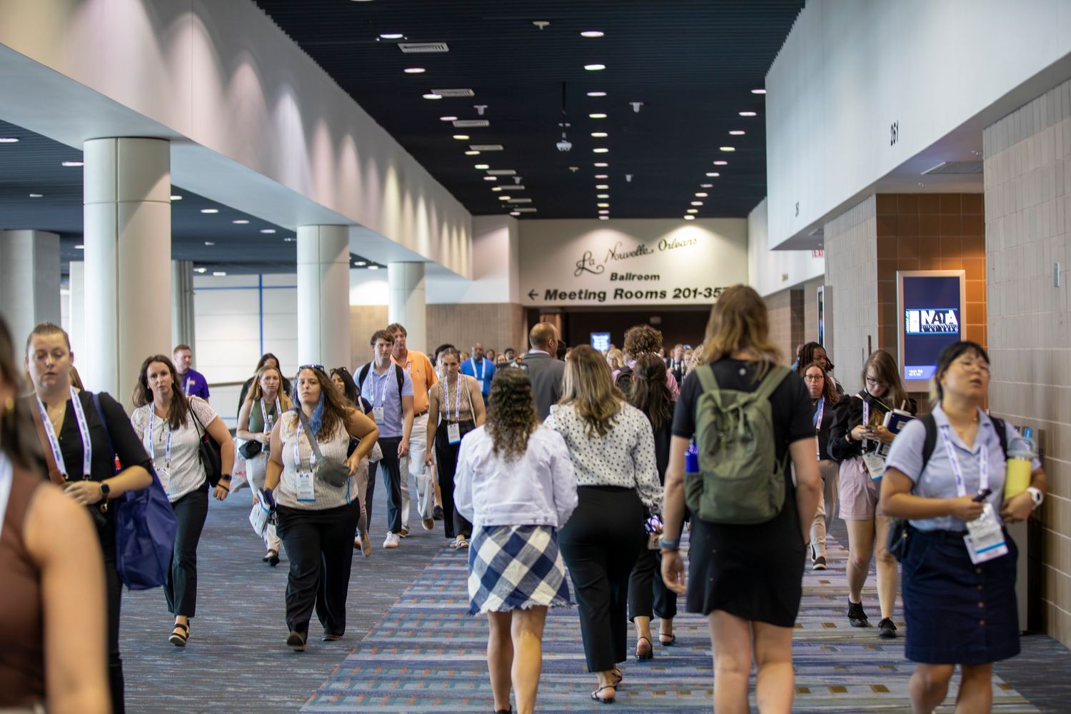 Busy convention center hallway filled with attendees walking and networking in a modern facility interior.