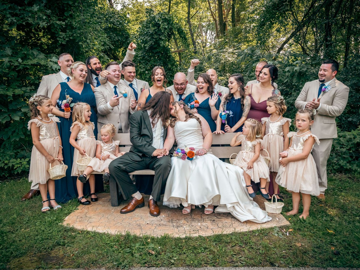 Large wedding party gathered outdoors for group photo with children in matching dresses.