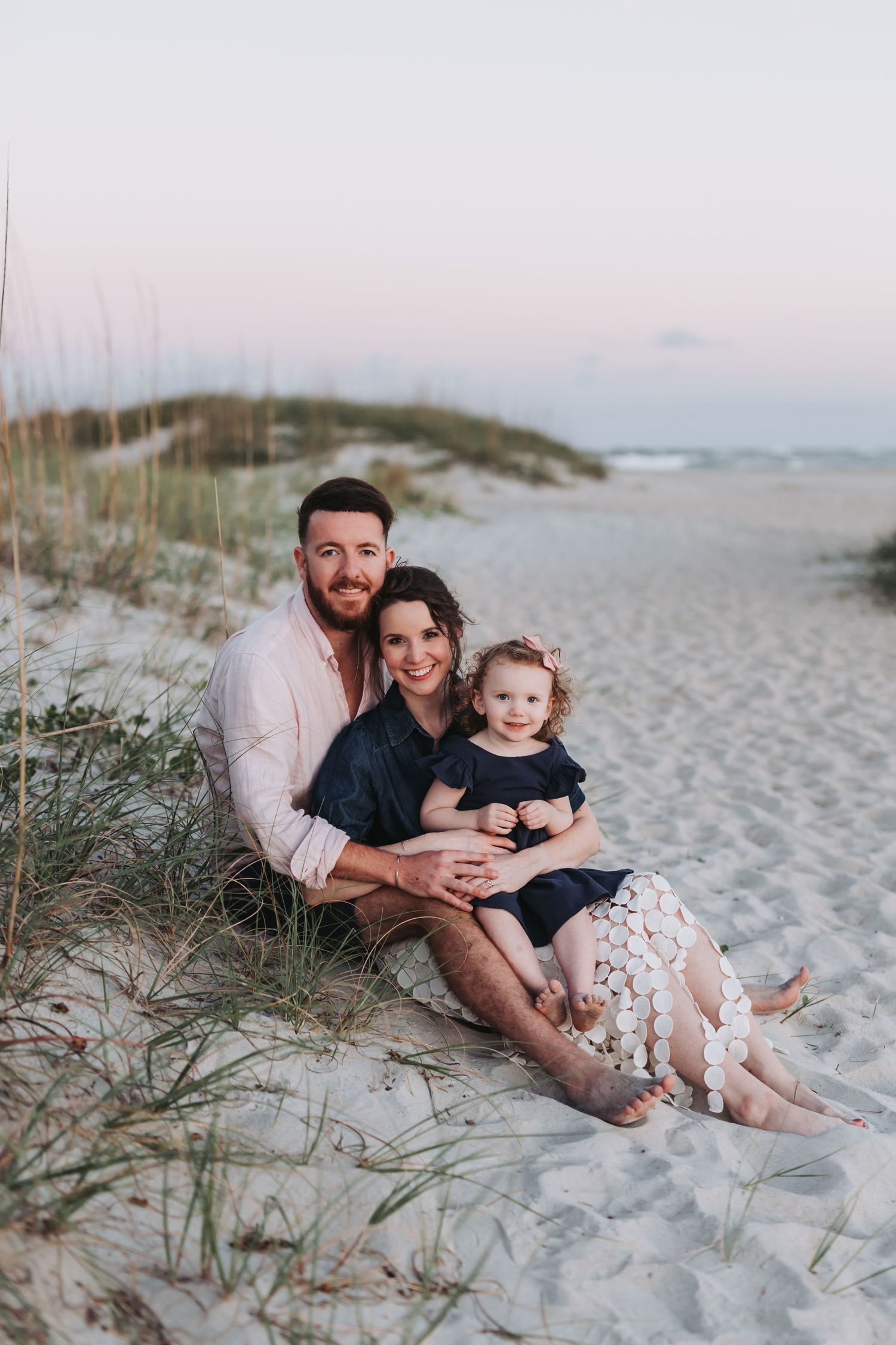 A family relaxes together on white sandy beach dunes during a sunset photoshoot.