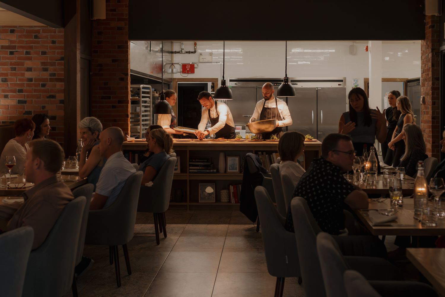 Warm ambiance of restaurant dining room with exposed brick walls and pendant lighting.