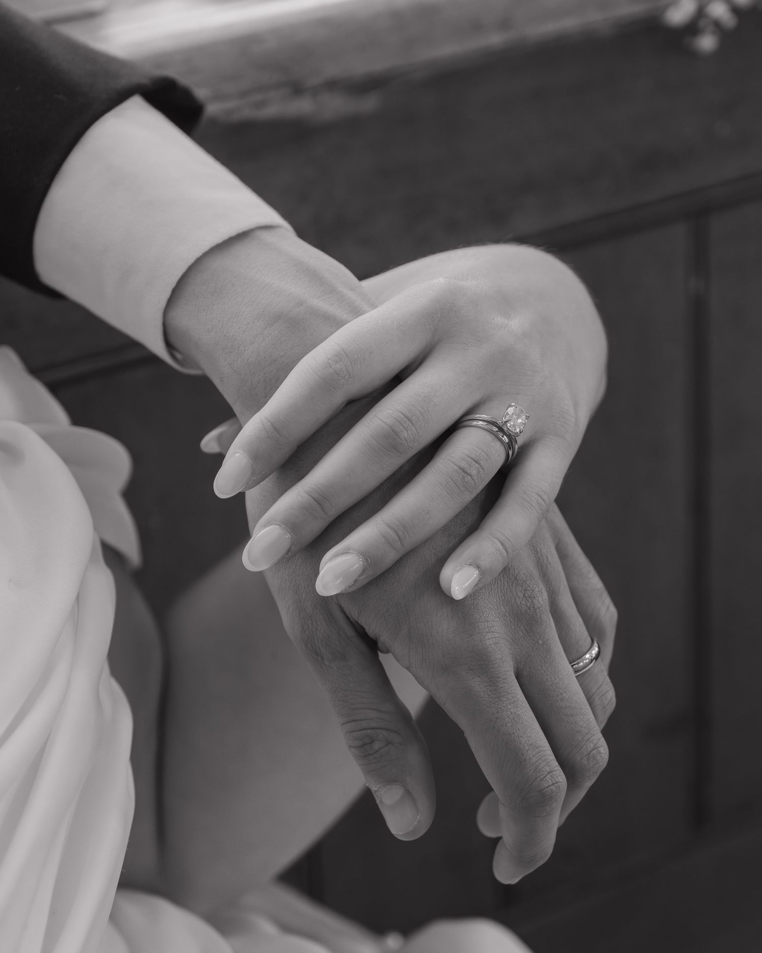 Close-up black and white photo of hands with engagement and wedding rings showing tender romantic moment.