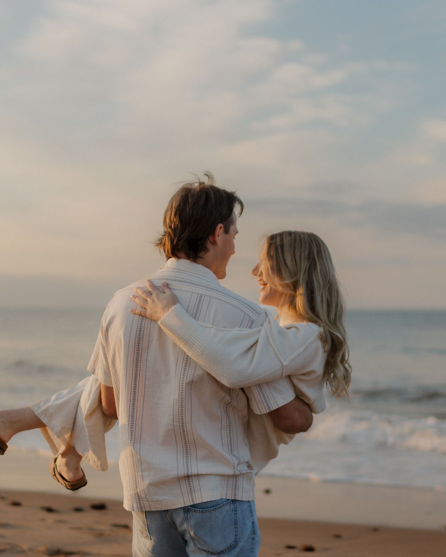 Romantic beach scene at sunset with couple embracing on sandy shore.