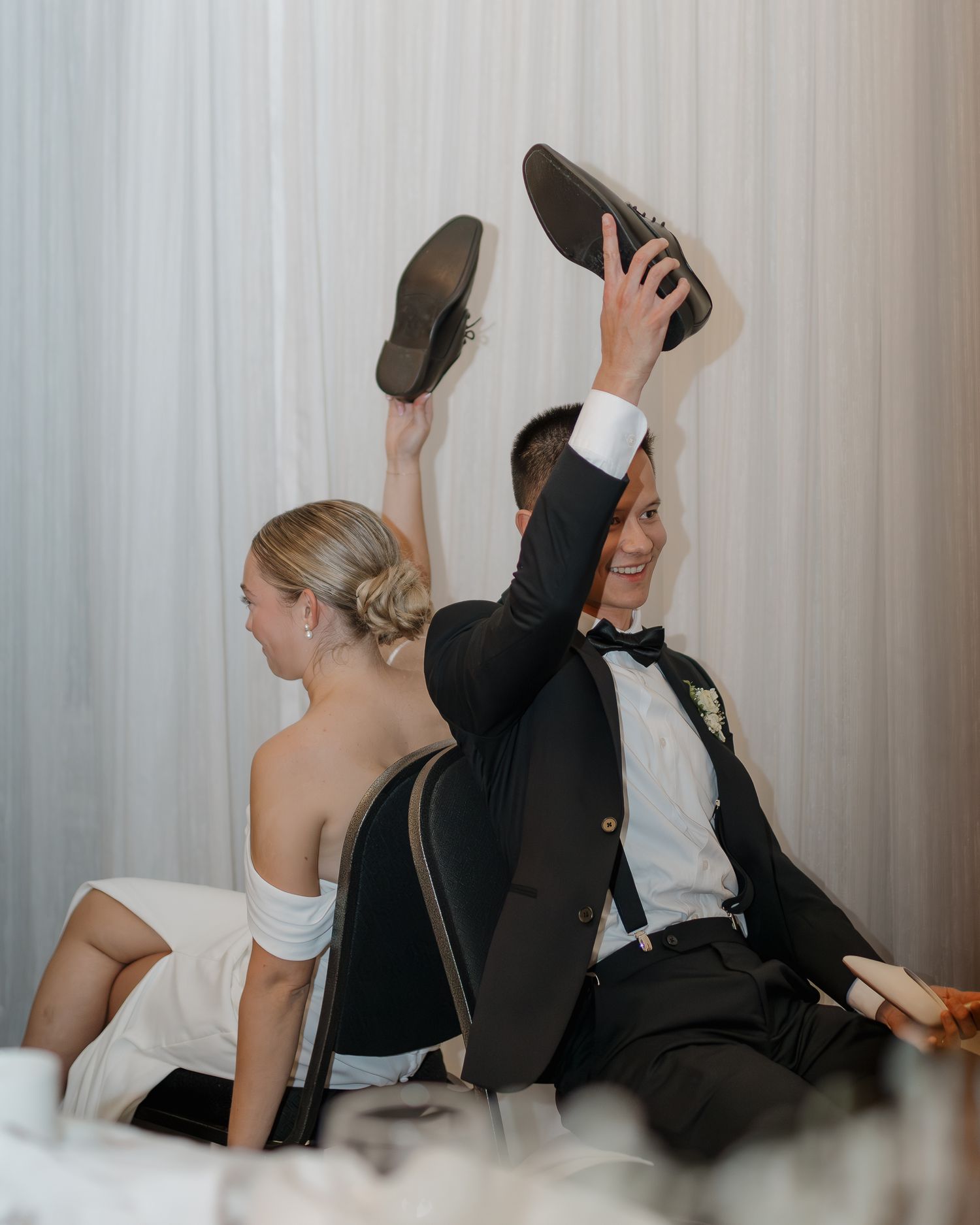 Playful wedding couple showing off their shoes in a fun candid moment.