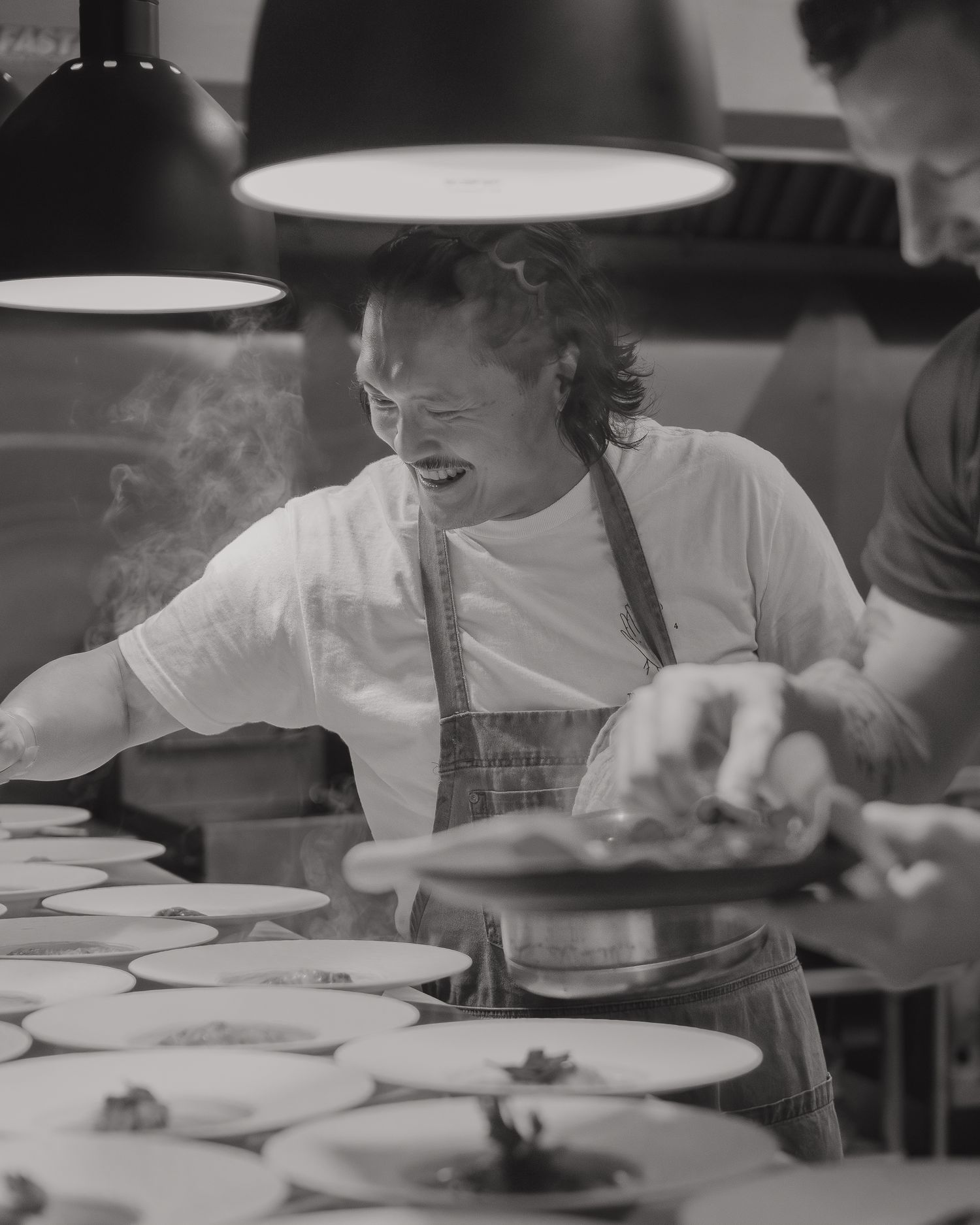 Black and white photo of chef working on multiple plates in restaurant kitchen.