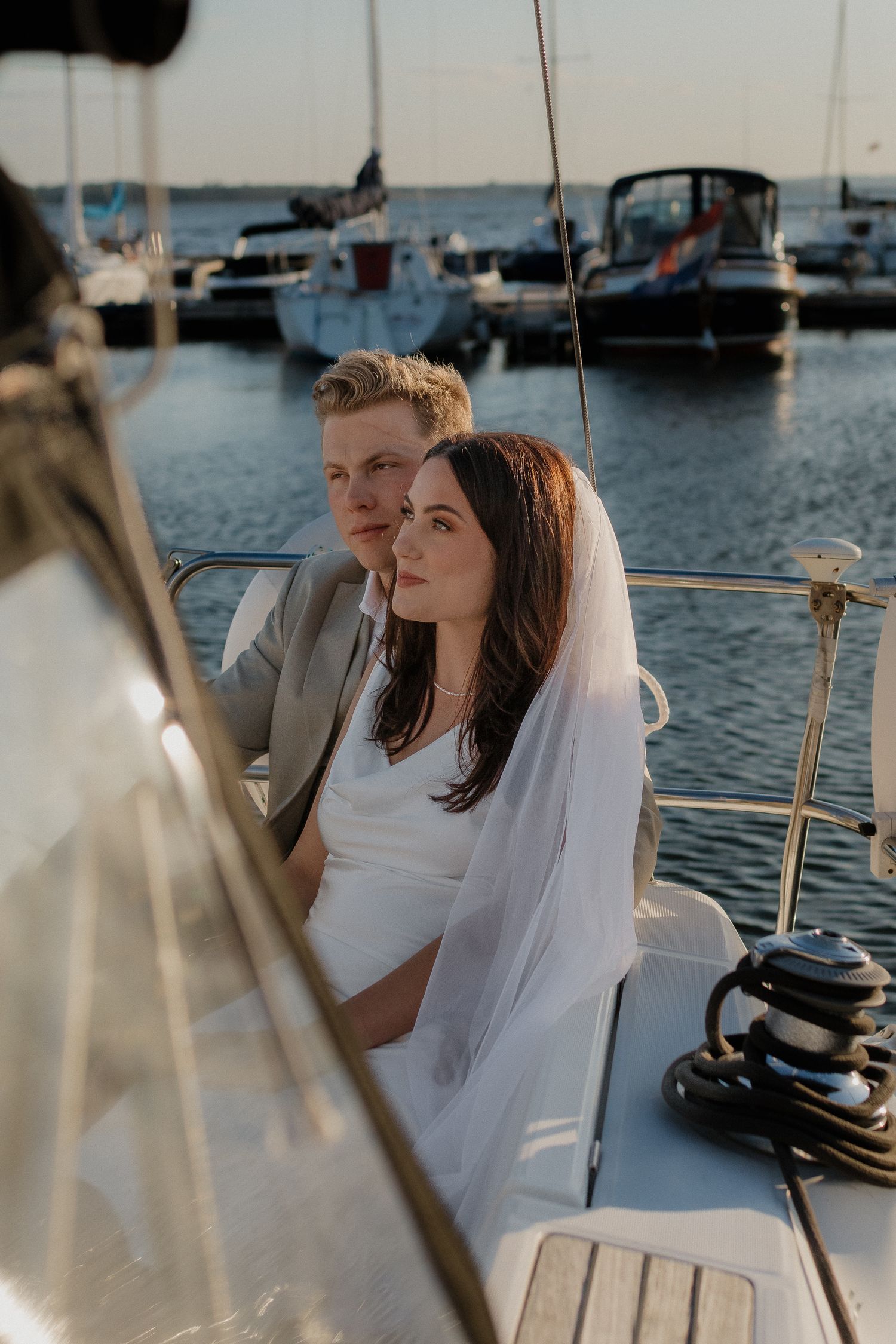 A couple celebrates their wedding day aboard a sailboat in a marina at sunset.