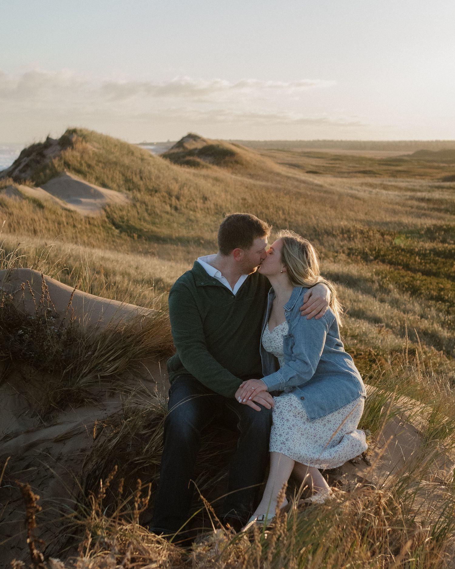 Romantic couple embracing on coastal dunes during golden hour.