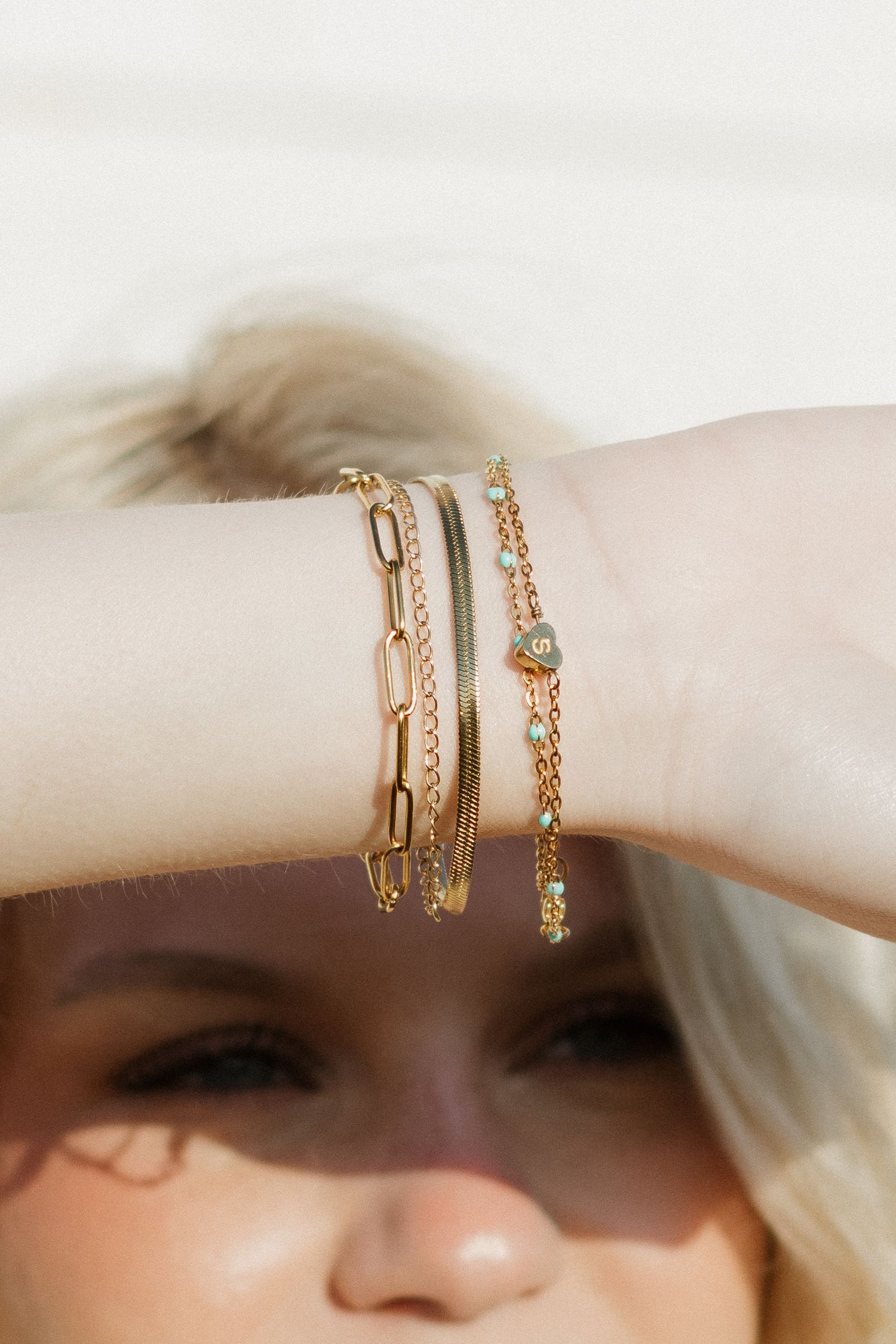 Gold chain link bracelets styled on wrist in warm sunlight.