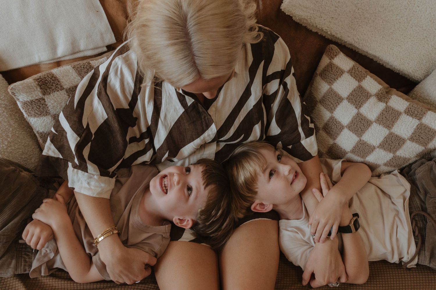 Two young people lying together peacefully on checkered pattern bedding in warm muted tones.