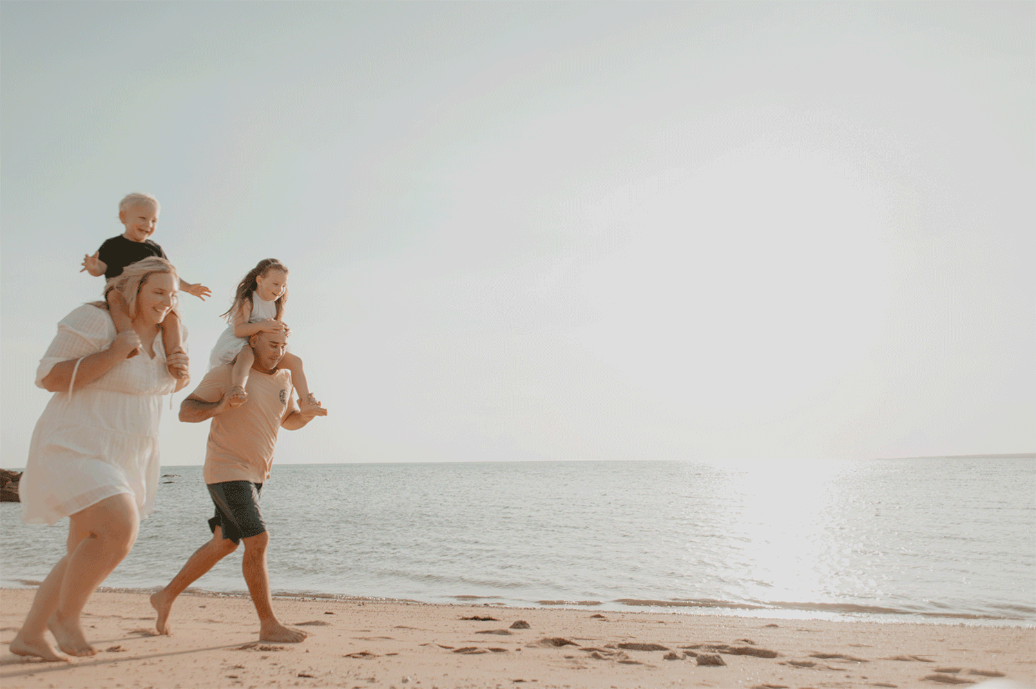 Two people in light clothing jog together along a peaceful beach at sunset with ocean waves in the background.