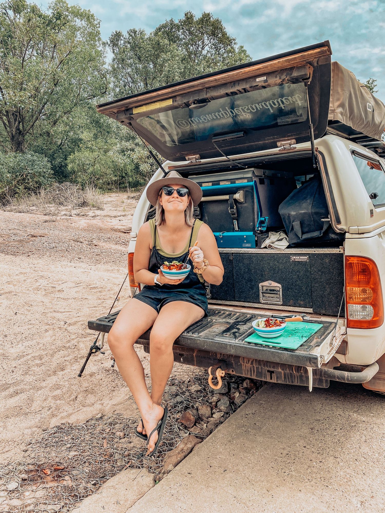 Camping setup with open truck tailgate showing camping gear and storage solutions in a remote outdoor location.