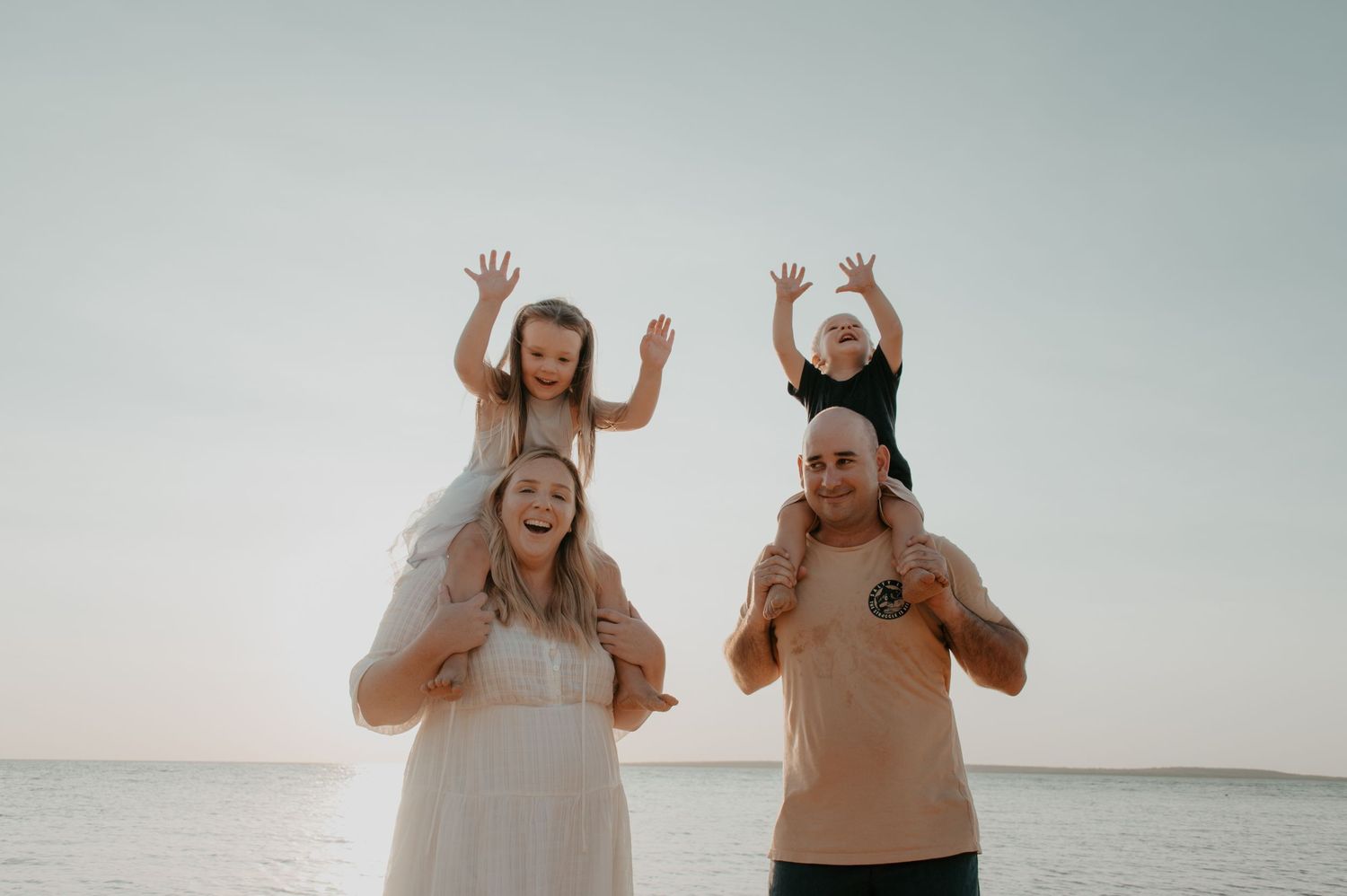 Happy family celebrates together on the beach at sunset with their arms raised in joy.