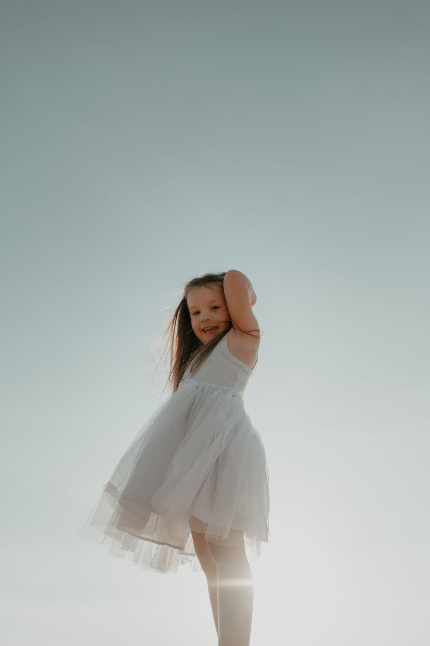 A person in a flowing white dress stands gracefully against a bright sky background with sunlight glowing behind them.