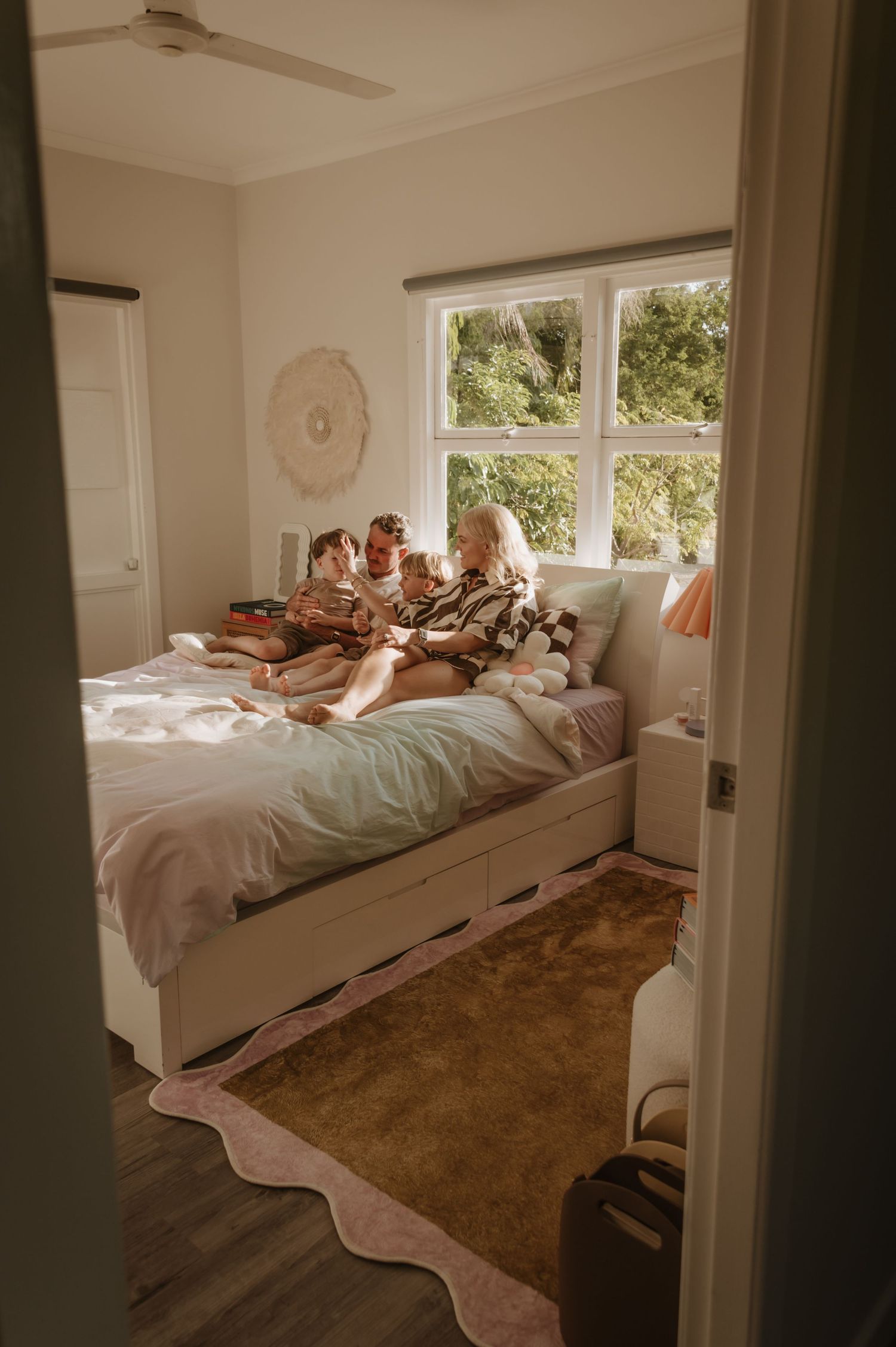 A cozy bedroom with white bedding, natural light from windows, and a brown rug on the floor in warm vintage tones.
