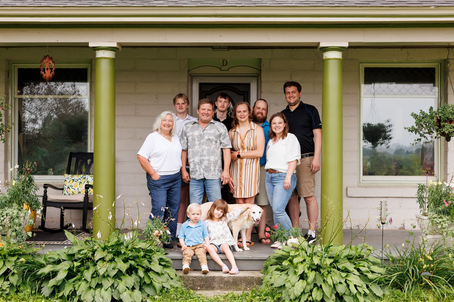 Extended family portrait on house porch steps with greenery and columns.
